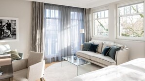 A modern hotel room with a sofa, a chair, a glass coffee table, and a bed. - Clounys Hotel & Restaurant (Hamburg)