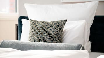 Una cama bien hecha con almohadas blancas y estampadas, una manta gris y un cabecero oscuro.