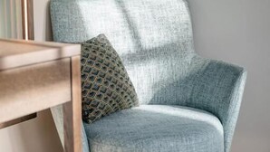 A light blue armchair with a patterned pillow, positioned next to a wooden chair and a table. - Clounys Hotel & Restaurant (Hamburg)