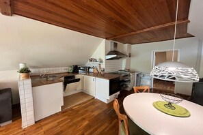 A compact kitchen with wooden flooring, white cabinetry, a built-in oven, and a hanging light fixture.