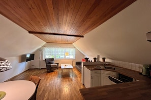 A compact living space with a dining area, a kitchen, and a seating area with a view of greenery outside.