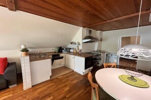 Una cucina moderna con mobili bianchi, soffitto in legno e zona pranzo con tavolo e sedie bianche.