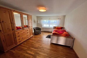 A bedroom with a wooden wardrobe, a single bed with a blanket, a chair, and a window with curtains. - Ferienwohnung, Wieck am Darß (Wieck am Darß)