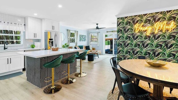 A modern kitchen with white cabinets, a central island with bar stools, and a dining area with a round table.