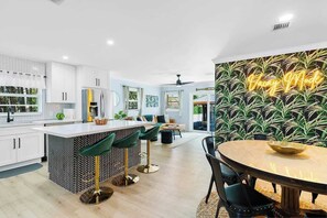 A modern kitchen with white cabinets, a central island with bar stools, and a dining area with a round table. - Luxury Spa/Golf Villa with Pool Table! (Dania Beach)