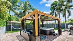 A covered outdoor seating area with a hot tub, a hammock, and a grill.