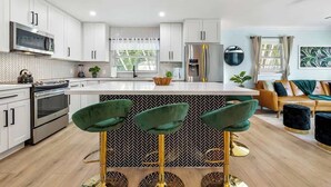 A modern kitchen with white cabinets, a central island, and a bar stool with green upholstery.