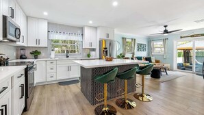 A modern kitchen with white cabinets, a central island with stools, and a dining area with a view.
