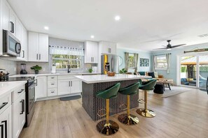 A modern kitchen with white cabinets, a central island with stools, and a dining area with a view.