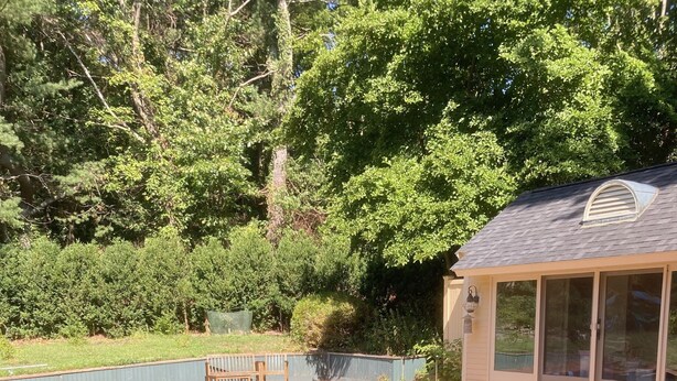A rectangular swimming pool with a brick border, surrounded by a wooden deck and a covered area with sliding glass doors. - Spacious vacation townhome unit with a pool (Weston)