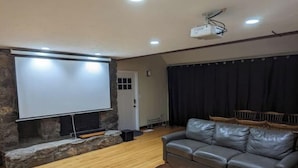 A living room with a stone fireplace, a large screen, a leather sofa, and a wooden coffee table. - Spacious vacation townhome unit with a pool (Weston)