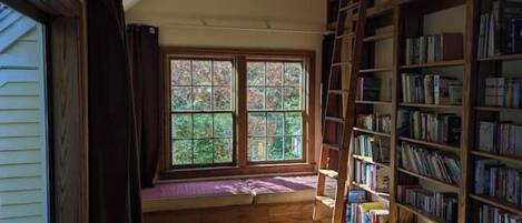 Um quarto com uma janela grande, uma escada de madeira e uma estante repleta de livros.
