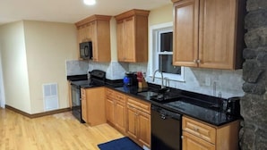 A kitchen with wooden cabinets, a black countertop, a built-in dishwasher, and a window above the sink. - Spacious vacation townhome unit with a pool (Weston)