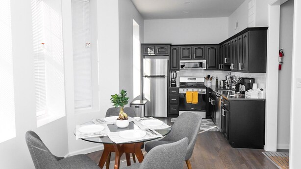 A modern kitchen with dark cabinets, stainless steel appliances, and a dining area with a round table and grey chairs.