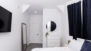 A modern bedroom with a bed, a bedside table, a mirror, a round mirror, and a dark curtain.
