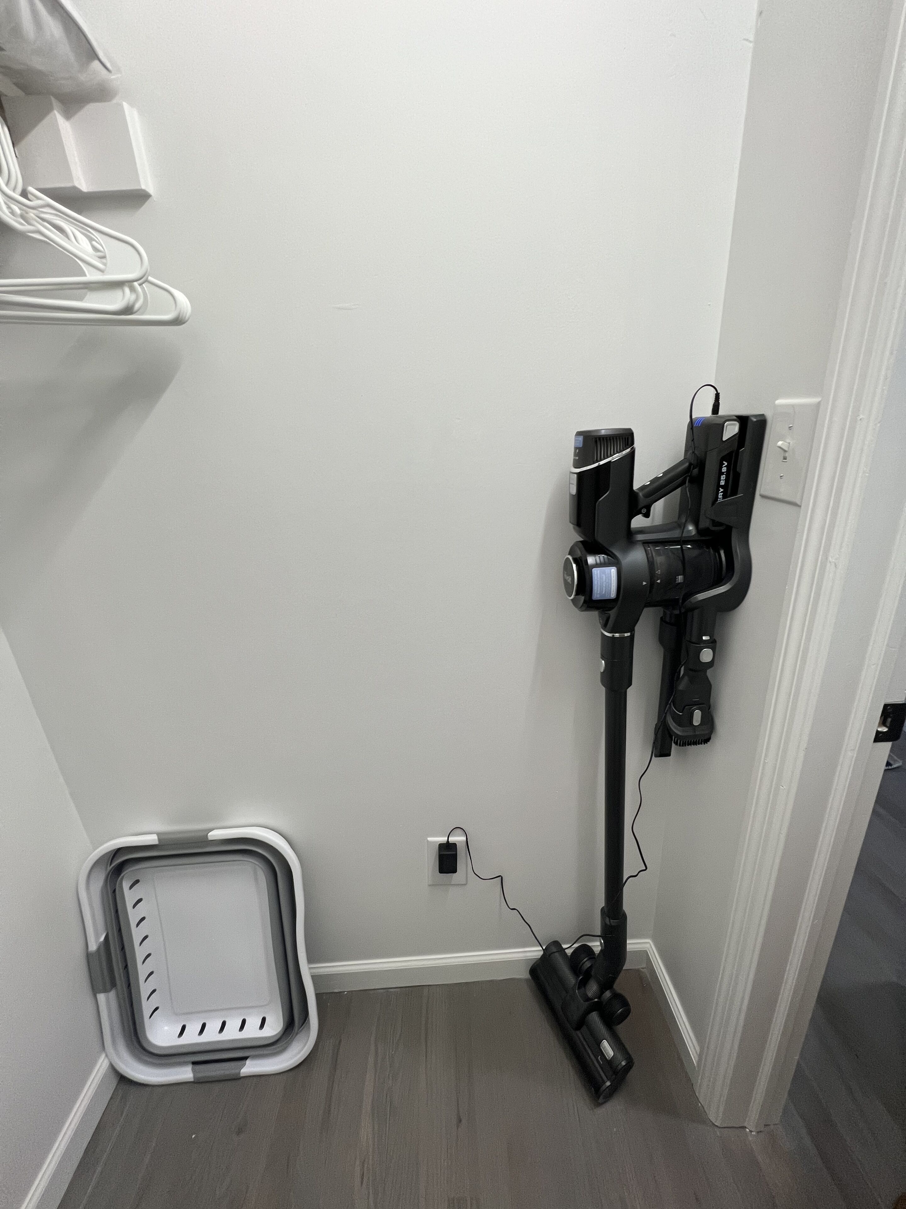 Un rincón de una habitación con una aspiradora, un enchufe y un cubo de basura.