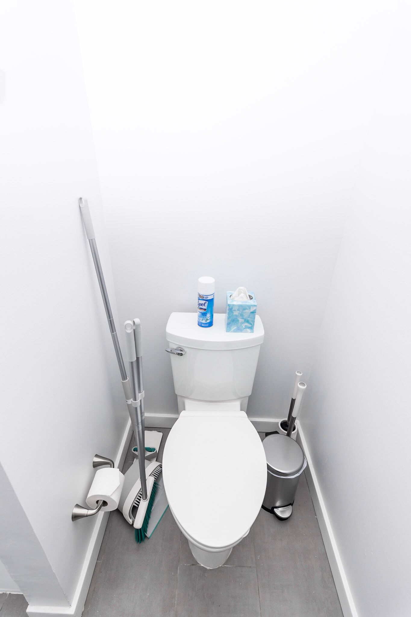 A clean, white bathroom with a toilet, a trash bin, a broom, and a mop.