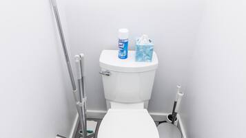A clean, white bathroom with a toilet, a trash bin, a broom, and a mop.