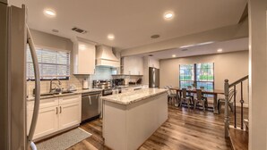 Una cocina moderna con armarios blancos, una isla central, electrodomésticos de acero inoxidable y un comedor con mesa y sillas de madera.
