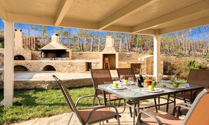 An outdoor patio with stone walls, a brick oven, and a table set for dining.