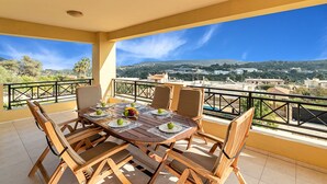 Ein Balkon mit Holztisch, gedeckt für vier Personen, Stühlen und Blick auf eine Stadt und Hügel.