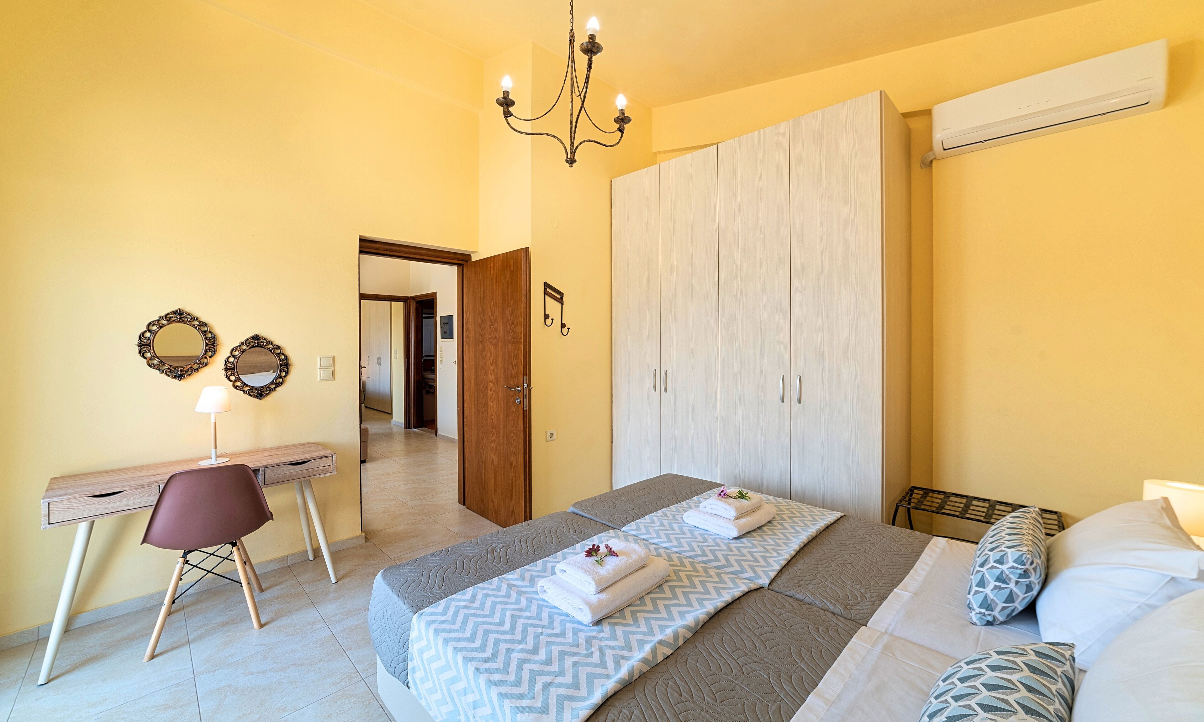 A bedroom with a bed, a desk, a chair, a wardrobe, and a chandelier.