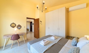 A bedroom with a bed, a desk, a chair, a wardrobe, and a chandelier.