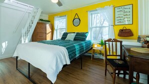 Un dormitorio con cama, una silla, escritorio, ventilador de techo y ventana con cortinas.