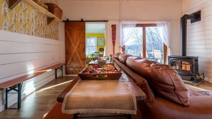Una sala de estar acogedora con un banco de madera, un sofá, una chimenea y una mesa de comedor con comida.