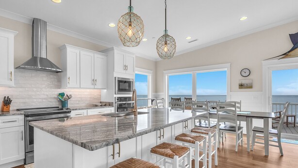A modern kitchen with white cabinets, a large island with bar stools, and pendant lighting. - The Sale Fish: Modern Oceanfront Home with Private Pool and Elevator (Oak Island)