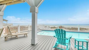 A wooden deck with a pool, a turquoise Adirondack chair, and a white fence overlooking the beach. - The Sale Fish: Modern Oceanfront Home with Private Pool and Elevator (Oak Island)