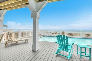 A wooden deck with a pool, a turquoise Adirondack chair, and a white fence overlooking the beach. - The Sale Fish: Modern Oceanfront Home with Private Pool and Elevator (Oak Island)