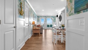 A hallway with white doors, a wooden floor, a dining area with a table and chairs, and a view through a glass door. - The Sale Fish: Modern Oceanfront Home with Private Pool and Elevator (Oak Island)