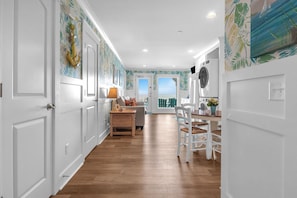 A hallway with white doors, a wooden floor, a dining area with a table and chairs, and a view through a glass door. - The Sale Fish: Modern Oceanfront Home with Private Pool and Elevator (Oak Island)