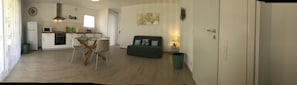 A compact living space with a kitchenette, a dining area with a glass table, and a sofa.