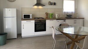Eine moderne Küche mit Mikrowelle, Herd, Backofen und Geschirrspüler. Ein Glastisch mit Stühlen, ein Fenster mit Vorhängen und eine Uhr an der Wand sind ebenfalls vorhanden.