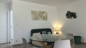Ein Essbereich mit einem runden Glastisch, vier Stühlen, einer Couch und einer Wandleuchte.