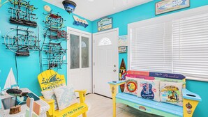 Een kamer met een turquoise muur, een witte deur, een bank met kleurrijke kussens, en een wandmontage voor surfplanken.