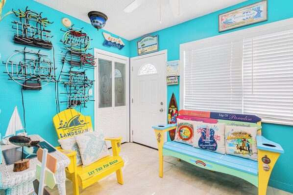 A room with a turquoise wall, a white door, a bench with colorful pillows, and a wall-mounted surfboard rack. - Walk to the pier and all attractions! Mermaid Manor (Daytona Beach)