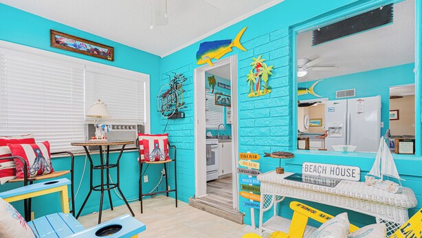 Een levendige kamer met een turquoise wand, een kleine tafel met stoelen, een bank en een bord met de tekst 