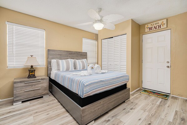 A bedroom with a bed, nightstand, lamp, ceiling fan, and a door with a sign. - Walk to the pier and all attractions! Mermaid Manor (Daytona Beach)