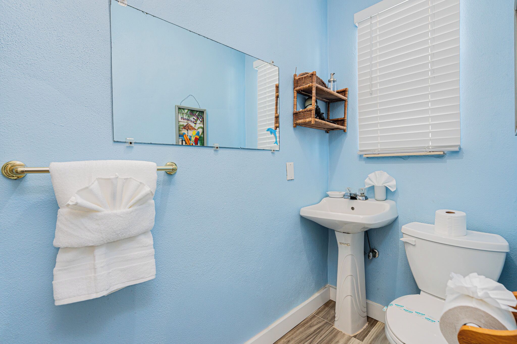 Un baño con pared azul, lavamanos blanco, inodoro y toallero.