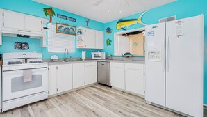 Een keuken met witte kastjes, een witte koelkast, een magnetron en een vaatwasser.