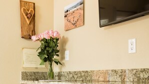 Eine Küche mit Granit Arbeitsplatte, einem braunen Stuhl, weißen Schränken, einer herzförmigen Dekoration, einem gerahmten Bild und einer Vase mit Blumen.