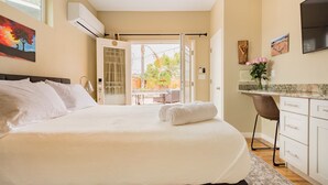 Ein Schlafzimmer mit einem großen Bett, einem Schreibtisch und einem Stuhl. Es gibt ein Fenster und eine Klimaanlage.