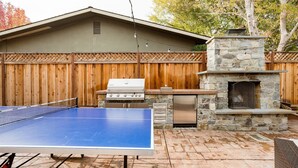 Ein Garten mit Pongtisch, Grill und Kamin aus Stein.