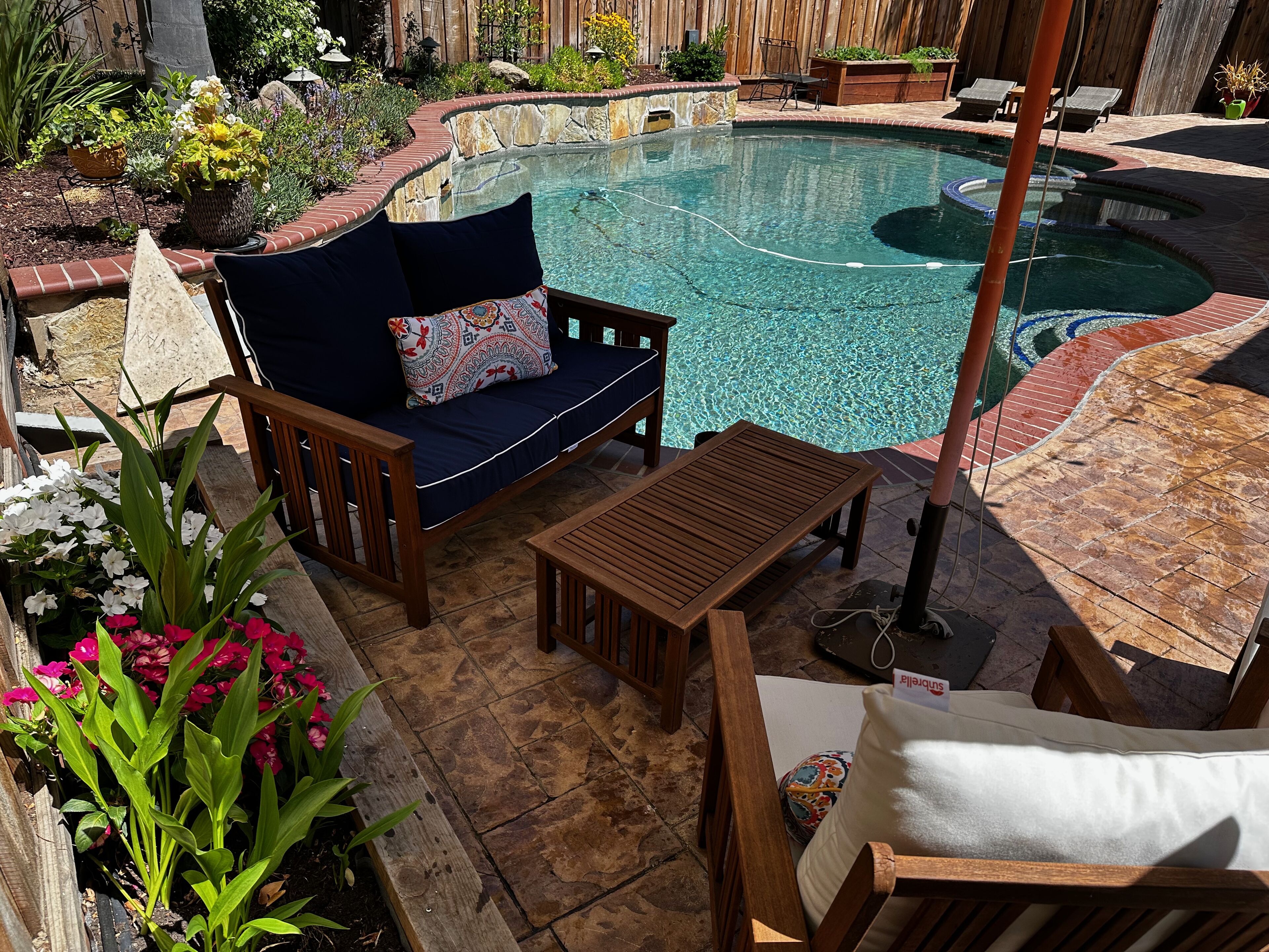 A backyard with a swimming pool, wooden deck, and outdoor furniture including a sofa and table.