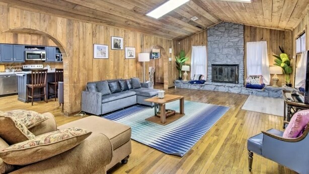 Amplia sala de estar con chimenea de piedra, techo de madera y área de cocina con electrodomésticos modernos.