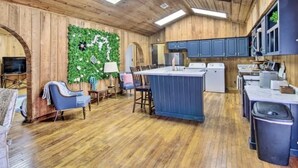 Un interior rústico con paredes de madera, un adorno verde en la pared, una zona de comedor y una cocina con armarios azules.