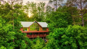 Una baita di tronchi immersa in una fitta foresta, con un'ampia vetrata e un balcone.